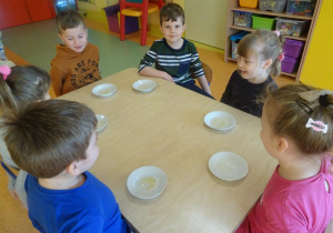 Dzieci siedzą przy stoliku przed każdym dzieckiem leży talerzyk z miodem.